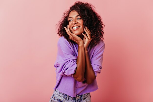 Enthusiastic female model posing on rosy with sincere happiness. Indoor portrait of african stylish girl.