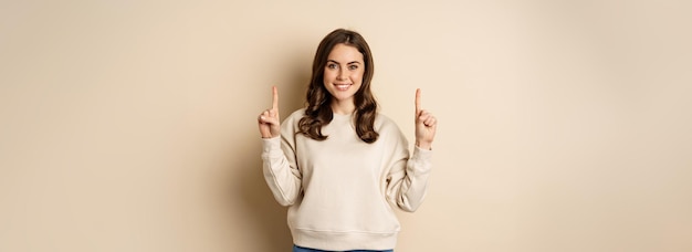 Бесплатное фото Восторженная девушка, указывающая пальцем вверх, показывает рекламный текст объявления или логотип вверх, стоя над