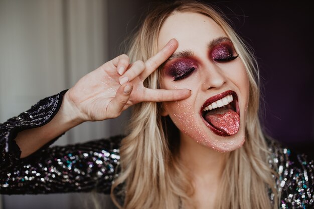 Enthusiastic girl with sparkle party makeup having fun. Indoor shot of gorgeous female model expressing sincere emotions.