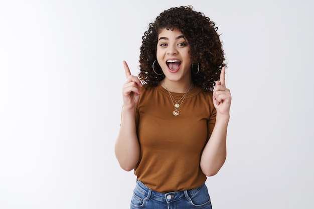 Enthusiastic good-looking curly european young woman open mouth wow yeah excited pointing up index fingers indicating upwards enthusiastic advertising awesome product, white background