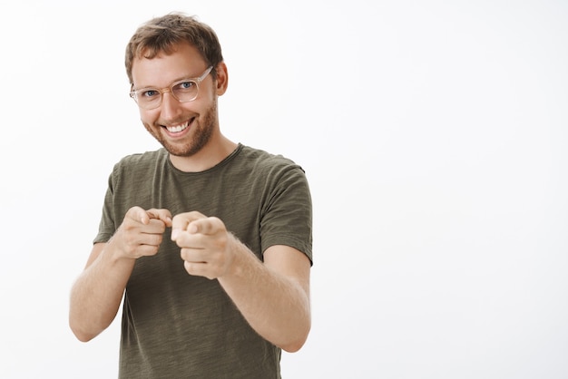 Enthusiastic happy and confident guy with bristle in glasses and dark-green t-shirt pointing with finger gun gesture as if picking candidate with broad satisfied smile