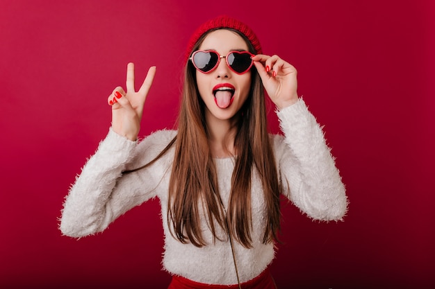 Enthusiastic long-haired girl wears cool sunglasses posing with peace sign