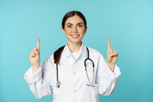 열광적인 의료 종사자 젊은 여성 의사가 광고 포인트를 보여주는 흰색 코트 청진기를...