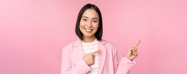 Enthusiastic professional businesswoman saleswoman pointing fingers right showing advertisement or company logo aside posing over pink background