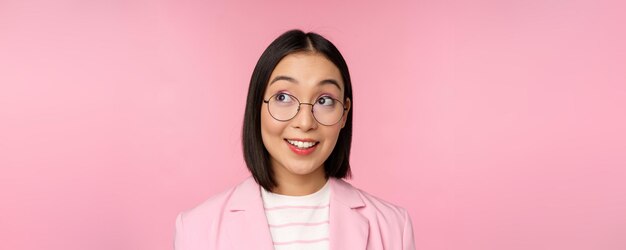 분홍색 배경 위에 서 있는 왼쪽 상단 로고 회사 광고에 흥미를 느끼는 안경을 쓴 열정적인 아시아 여성 여성 사업가