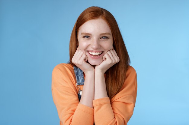 Enthusiastic sassy good-looking redhead caucasian girl lean head palms look amused intrigued listen interesting story pleased smiling laughing silly jokes standing blue background excited happy