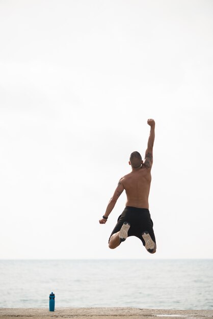 Enthusiastic sporty man jumping on shore