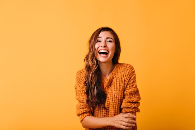 Enthusiastic white girl with long shiny hair laughing on orange. Excited european woman posing with sincere smile.