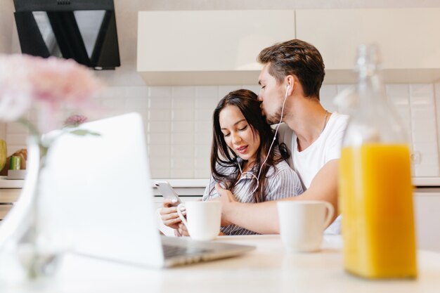 Free photo enthusiastic woman listening music and using smartphone while her boyfriend kissing her