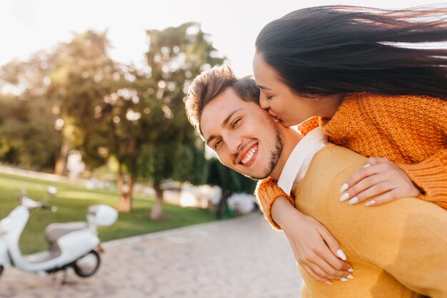 Enthusiastic woman with white manicure kissing laughing man in orange attire