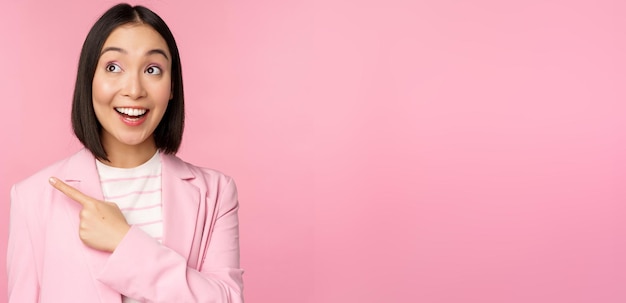 熱狂的な若いアジアの実業家のオフィスの従業員の人差し指は、広告ピンクの背景を示す幸せな笑顔でバナー広告を見て左