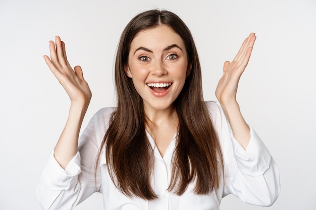 Enthusiastic young woman celebrating smiling and raising hands up in rejoicing winning and triumphin...