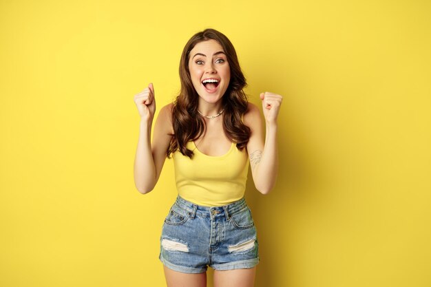 Enthusiastic young woman shouting and cheering rejoicing raising hands up and screaming in joy chant...