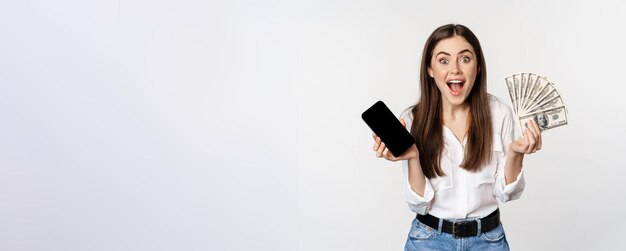 熱狂的な若い女性がお金を獲得し、スマートフォン アプリのインターフェイスと現金のマイクロクレジット賞 c を示します