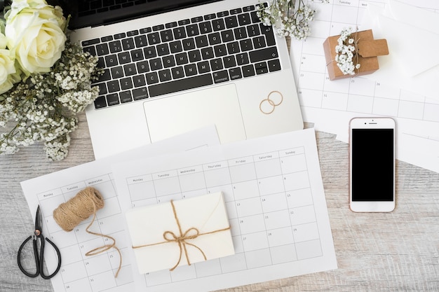 Конверт; календарь; ноутбук; цветы; смартфон; золотник; ножницы и спиральный ноутбук на деревянном столе