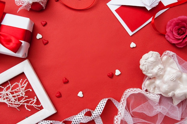 봉투, 선물, 심장, 장미, 천사, 발렌타인 데이를 위한 리본은 복사 공간이 있는 빨간색 배경에 평평하게 놓여 있습니다.