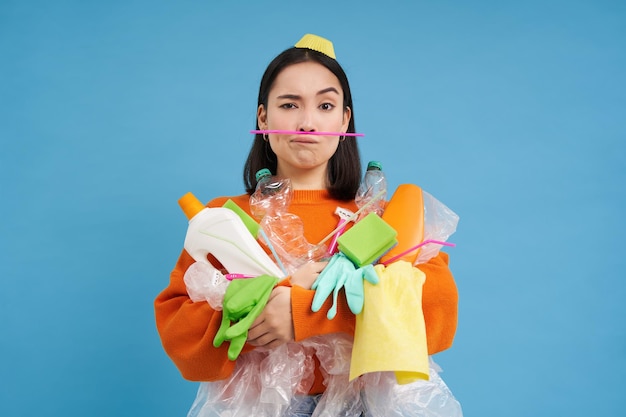 無料写真 ゴミの青い背景があるプラスチック廃棄物の山を持つアジアの女性の環境と生態学のポートレート