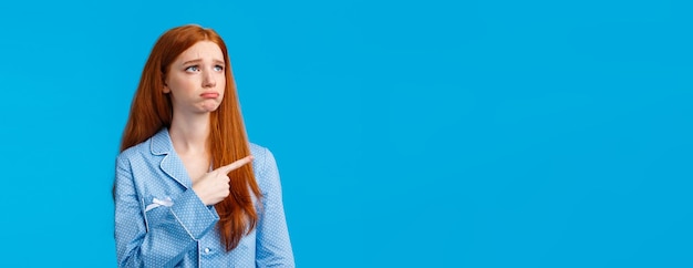 Foto gratuita invidia e triste ragazza adolescente rossa lunatica imbronciata in indumenti da notte che guardano e indicano l'angolo in alto a sinistra