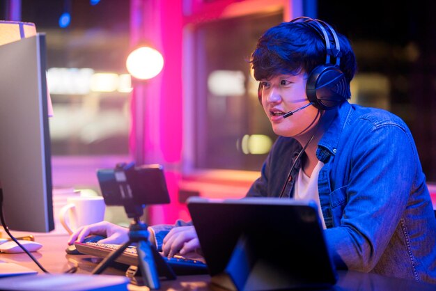 Esport online game streaming asian male wear headset play dogital metaverse cyber space online match compettition sport game battle night timeyoung asia male enjoy exited gamer successful celebration