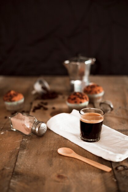 Espresso coffee in glass on white napkin with cocoa shaker and wooden spoon