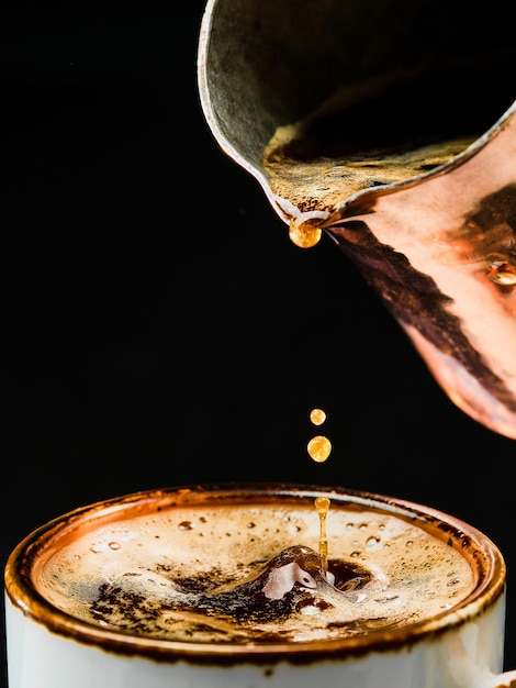 エスプレッソの詳細。コーヒーポットから白いカップにコーヒーを注ぐクローズアップ、選択的な焦点。バー、パブ、レストランでコーヒーを作るというコンセプト。ジェズヴェでコーヒーを淹れる。