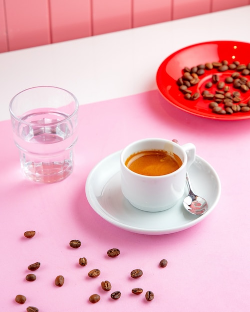 Foto gratuita caffè espresso con bicchiere d'acqua e chicchi di caffè sul tavolo