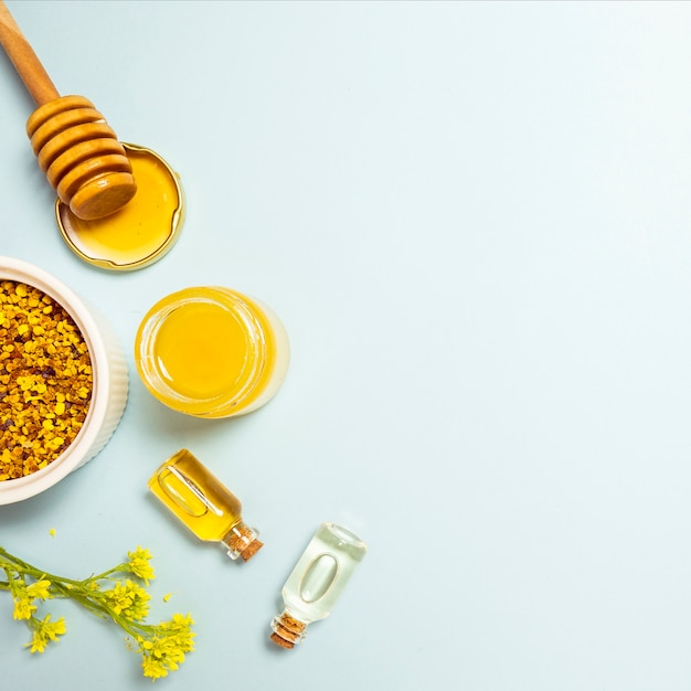 Free photo essential oil; bee pollen and honey with yellow fresh flower on blue backdrop