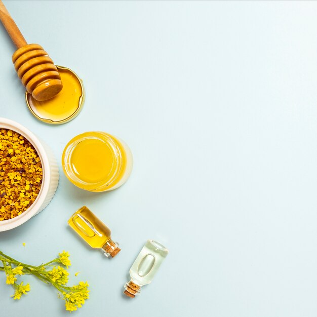 Эфирное масло; пчелиная пыльца и мед с желтым свежим цветком на синем фоне