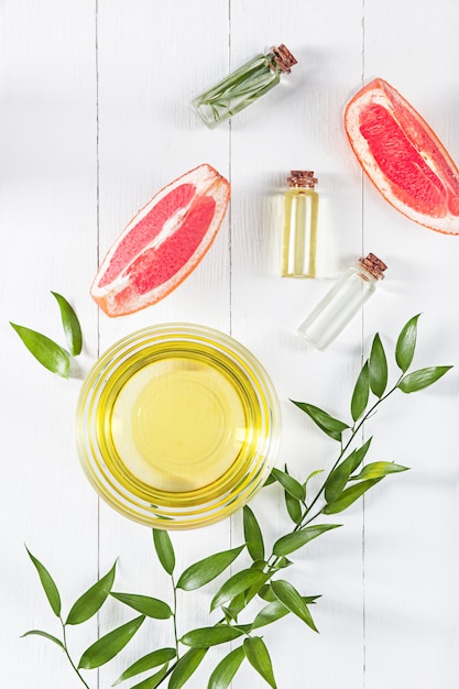 Essential oil in glass bottle with fresh, juicy grapefruit and green leaves-beauty treatment.