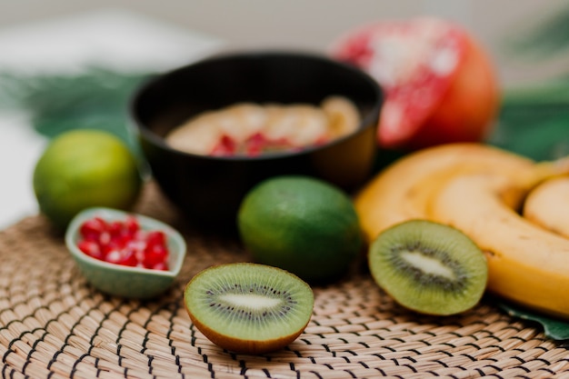 Essentials for cooking smoothie bowl. Blake plate topped with Kiwi, banana, pomegranate seeds, lime, granola, chia seeds. Healthy breakfast. Tropical mood.