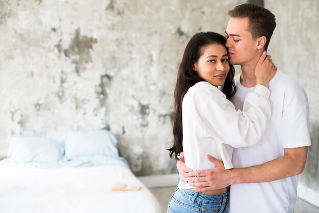 Ethnic female hugging boyfriend and looking at camera