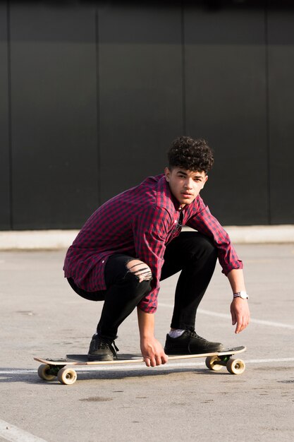 Ethnic hipster in checkered shirt riding skateboard squatting