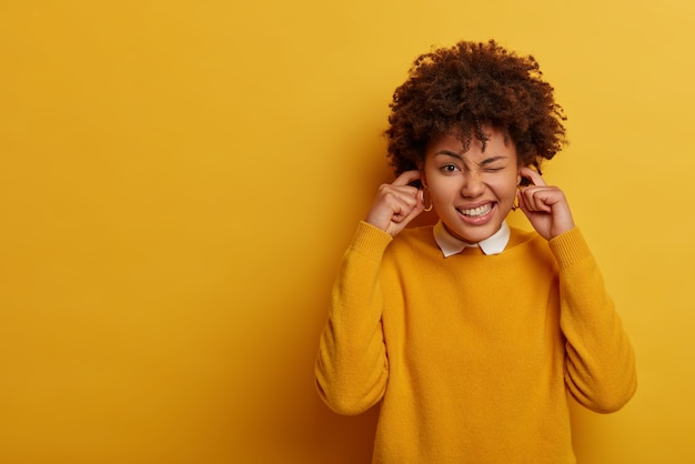 Free photo ethnic lady screws up eyes, complains on loud music, plugs ears