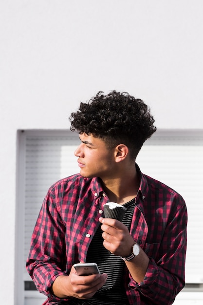 Ethnic male in checkered shirt holding ice cream and phone