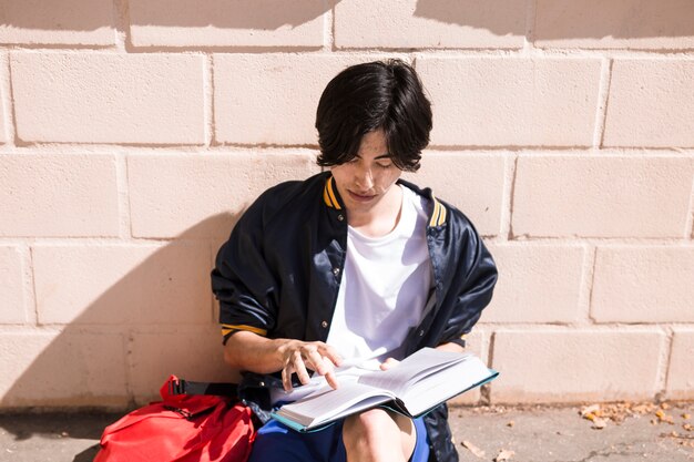펼친 책으로 아스팔트에 앉아 민족 학생
