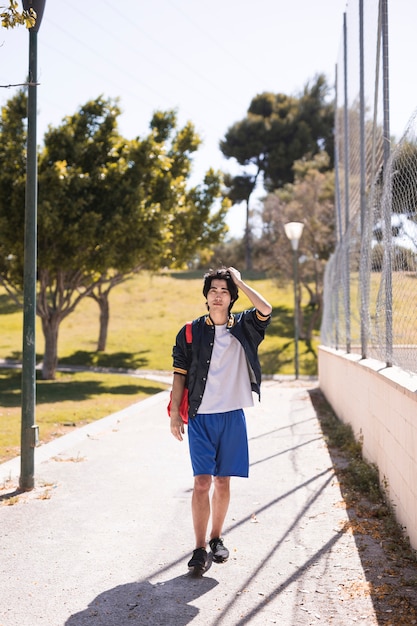 Ethnic schoolboy holding hair in park