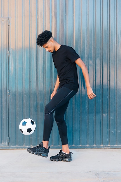 Ethnic sportsman kicking football on street