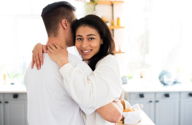 Ethnic young female hugging boyfriend and looking at camera