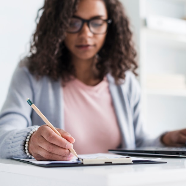 Ethnic young female writing on clipboard