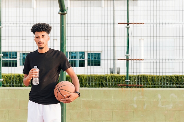 Ethnic young male holding basketball at court 