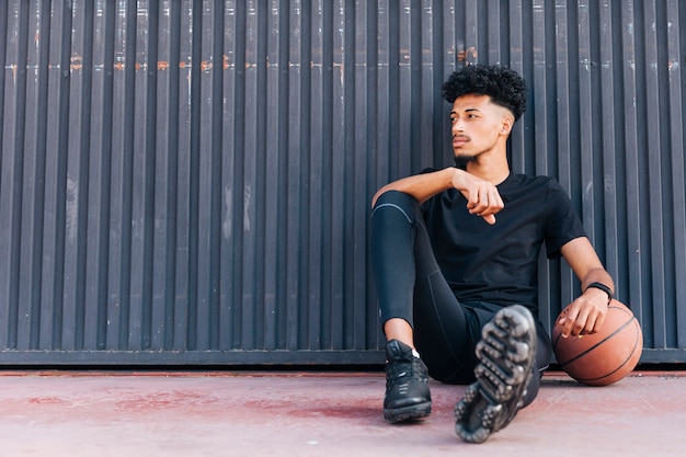 Ethnic young male sitting on ground with basketball 