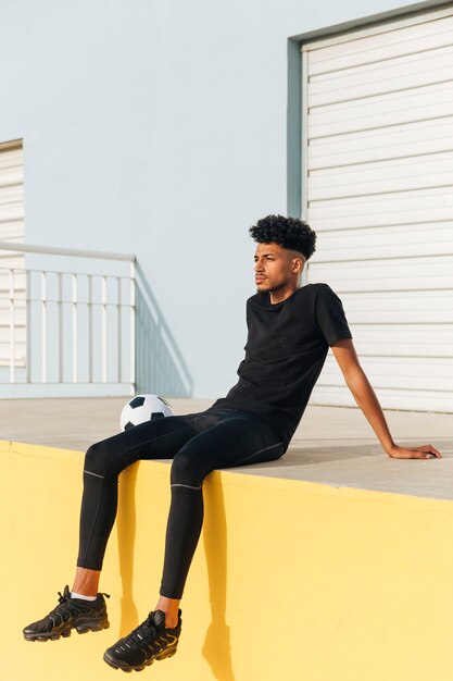 Ethnic young man sitting with soccer ball and dreaming 