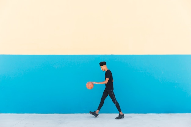 Ethnic young man in sports suit dribbling basketball