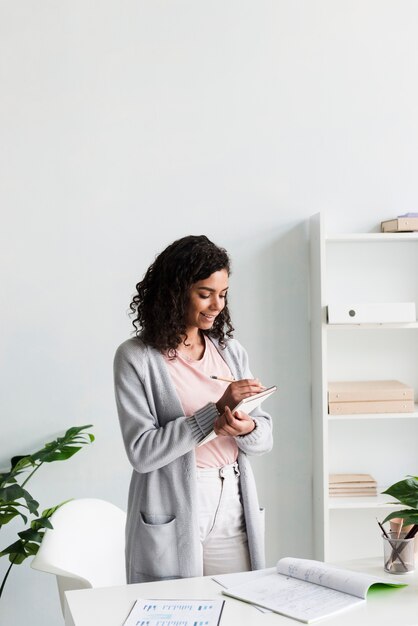 ethnic young woman writing on clipboard in office