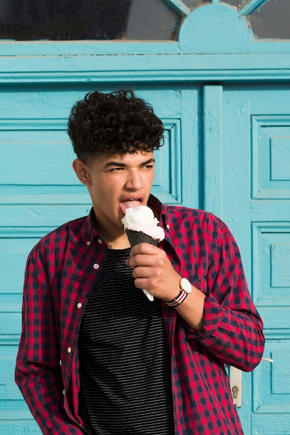 Giovanotto etnico che mangia il gelato in camicia a quadretti