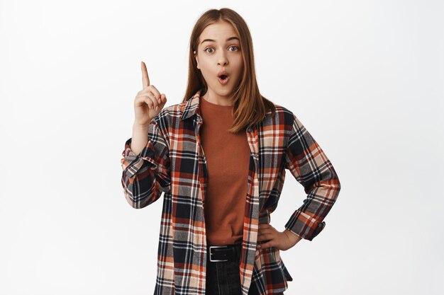 Eureka. Young excited woman gasp in awe, pointing finger up with surprised and impressed face, showing smth interesting, banner or logo upwards, white background.