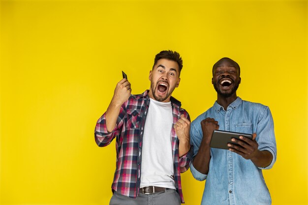 European and afroamerican guy are sincerely excited with the tablet and credit card in hands