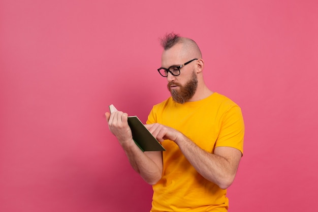 European bearded adult man in glasses read book isolated on pink