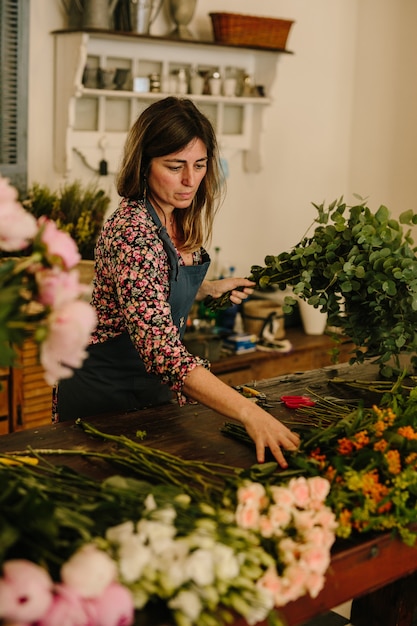 花柄のデザインスタジオで生け花を作る緑のエプロンを持つヨーロッパの女性花屋