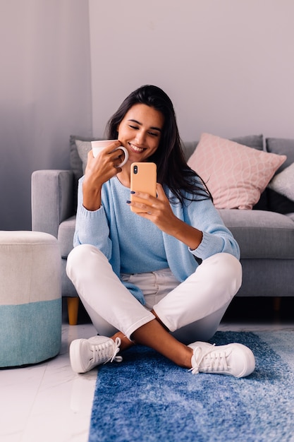 European fit brunette fashion blogger woman sits on floor in living room near sofa